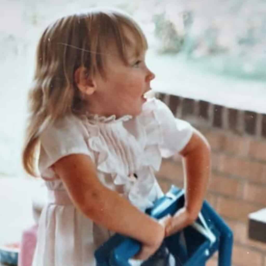 profile of a young girl with blonde hair, wearing a white ruffled dress, holding a blue object with an expression of excitement