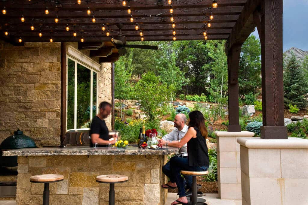 outdoor bar and grill area with a pergola overhead strung with bistro lights