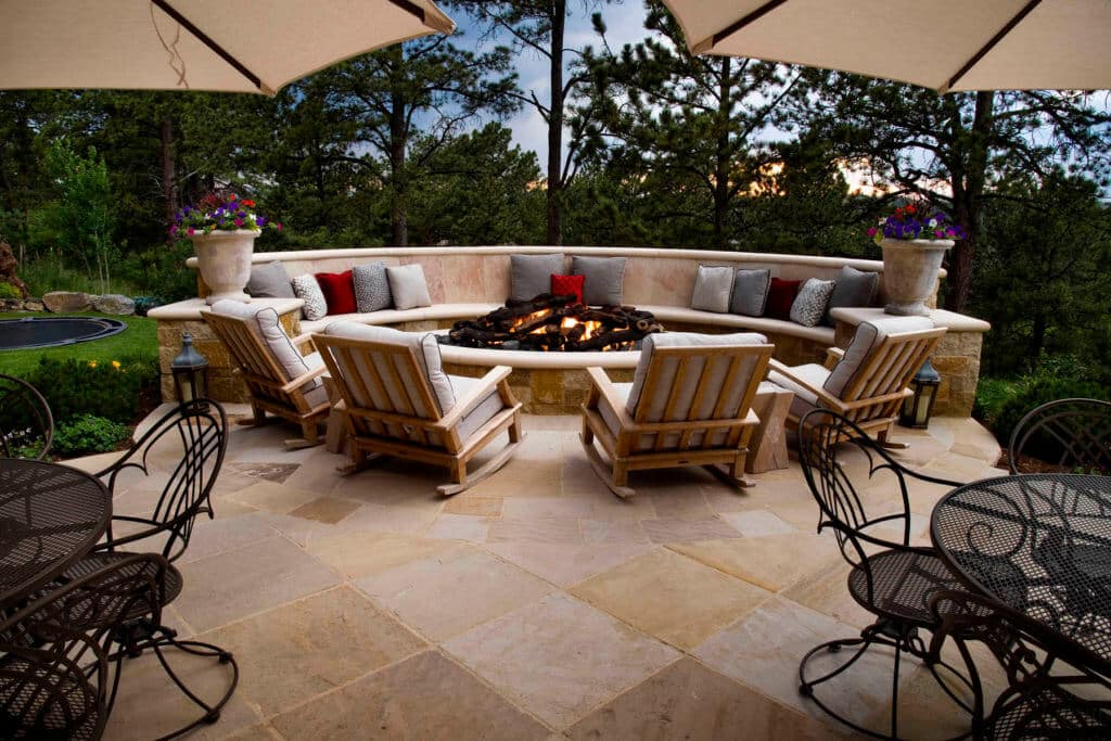 outdoor stone patio with built-in curved seating around a fire pit and additional rocking chairs