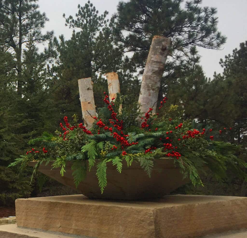 large stone planter with birch logs, evergreen boughs, and red berries