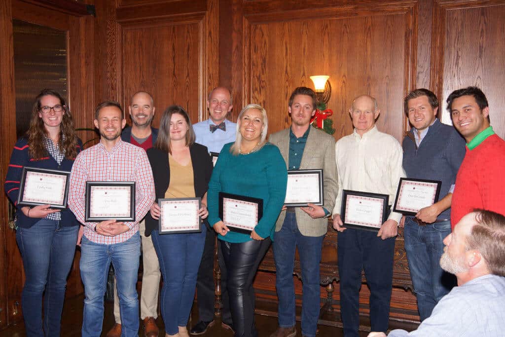 group of people holding framed certificates in front of wood paneled wall