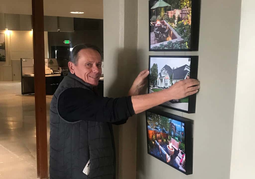 smiling man hanging framed landscape and home photos on a wall in an office setting