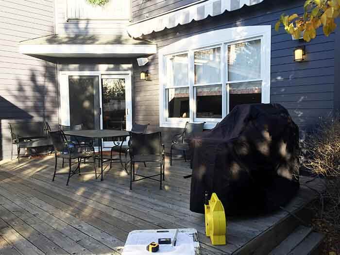 outdoor wood deck with a dining table and chairs, a large window, a sliding glass door, and a covered grill in the foreground