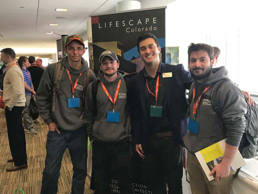 four young men posing next to a Lifescape Colorado banner at a conference or trade show