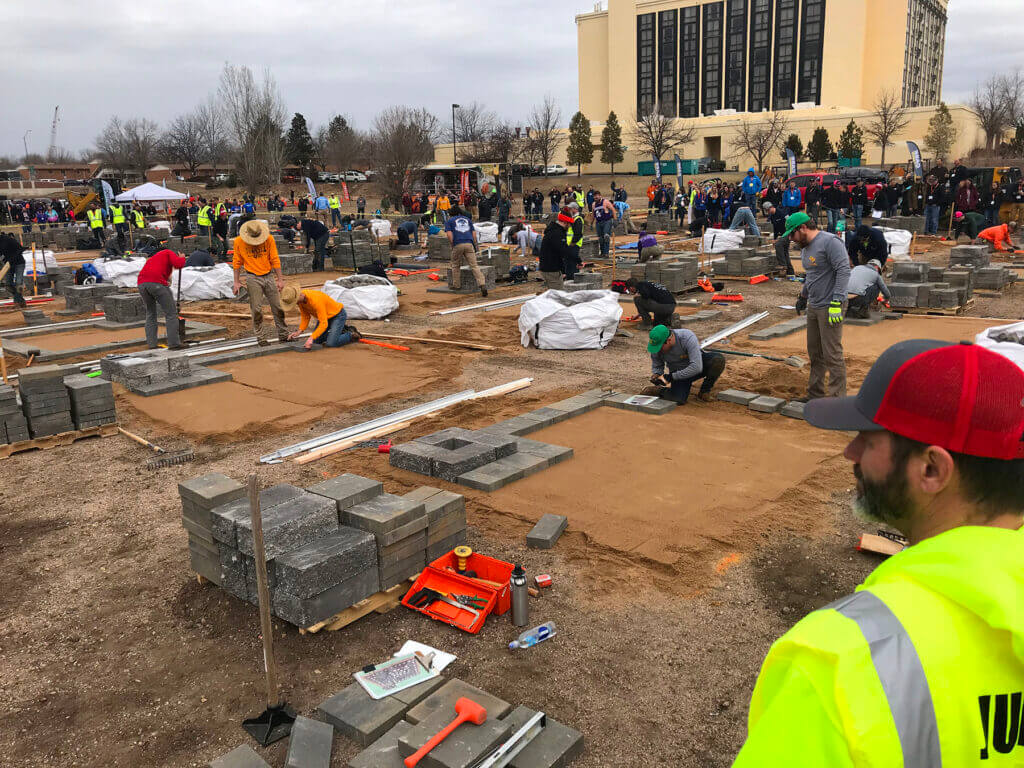 large group of construction workers and laborers installing concrete pavers on a sandy base in a competition setting
