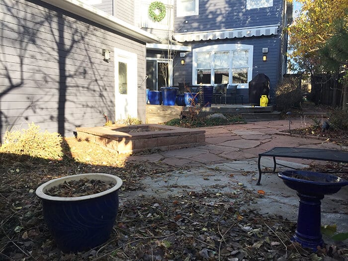 backyard with stone patio, raised stone planting bed, and a large blue planter and birdbath in the foreground, with a blue house in the background