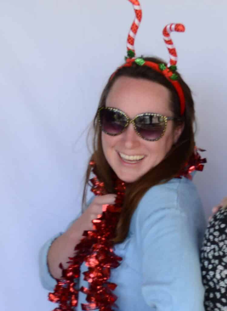 smiling woman wearing novelty sunglasses and a candy cane headband, draped with red tinsel