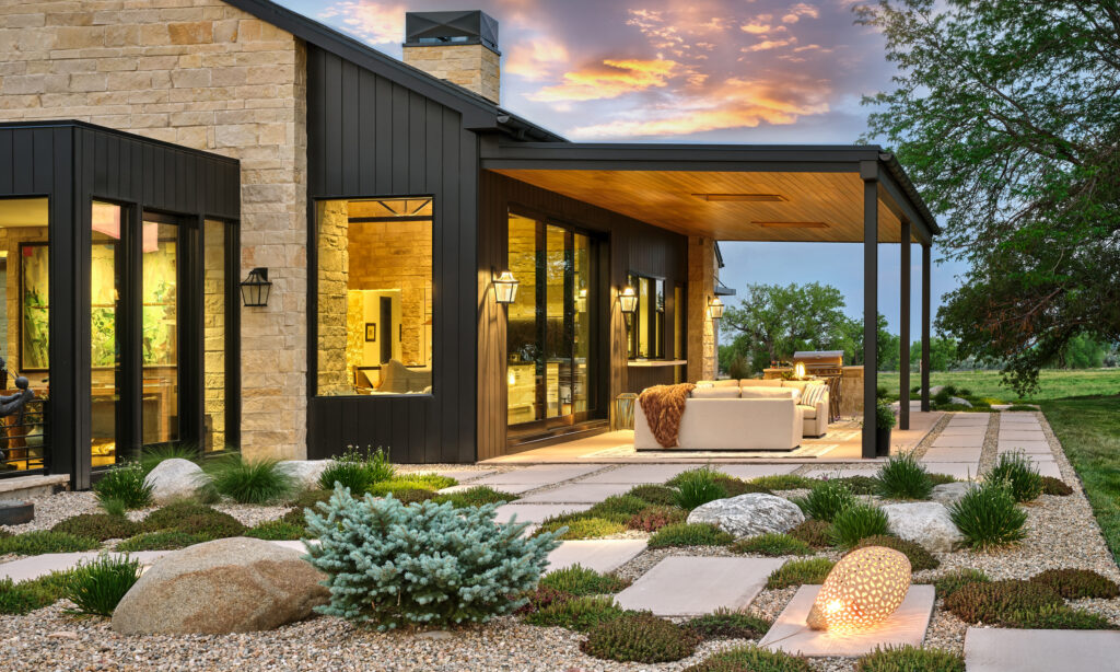Modern stone and black-paneled Colorado home with covered patio and xeriscape rock garden at sunset