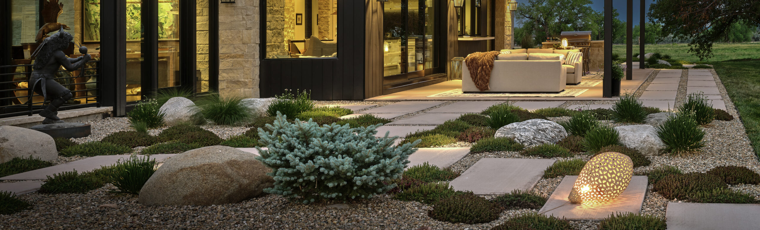 Colorado xeriscape patio at dusk with boulders, native grasses, and illuminated outdoor living space